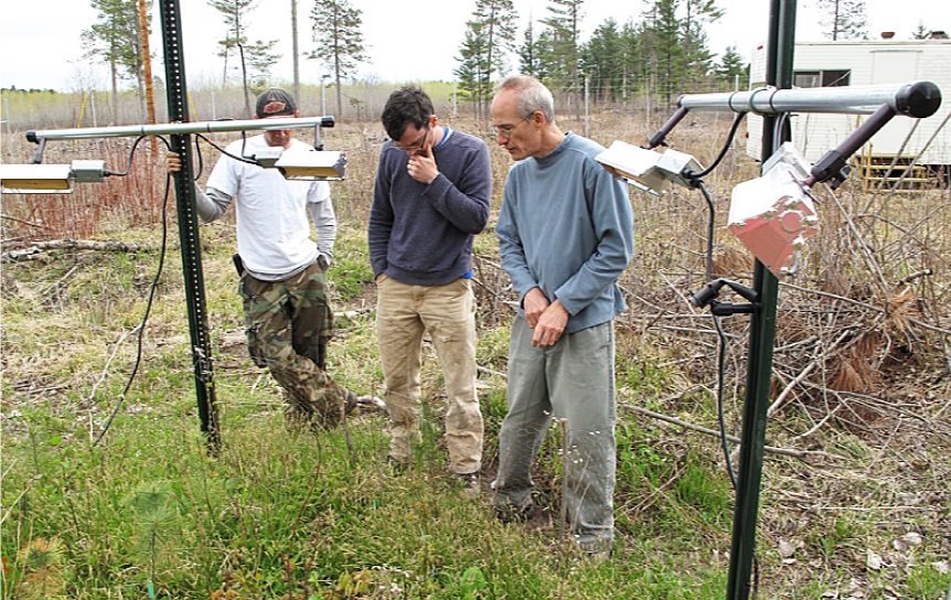 Three researchers are looking down at vegetation, surrounded by instruments and equipment.